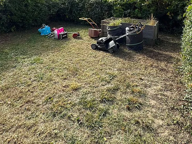 Garden after: lawn mown, a lawnmower and garden bags stand by the raised bed